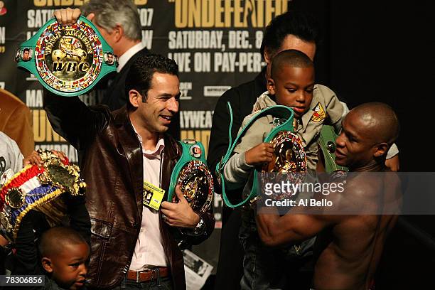 Floyd Mayweather Jr. Picks up his son Koraun Mayweather as IRL driver Helio Castroneves holds onto two of Mayweather's belts during the weigh-in for...