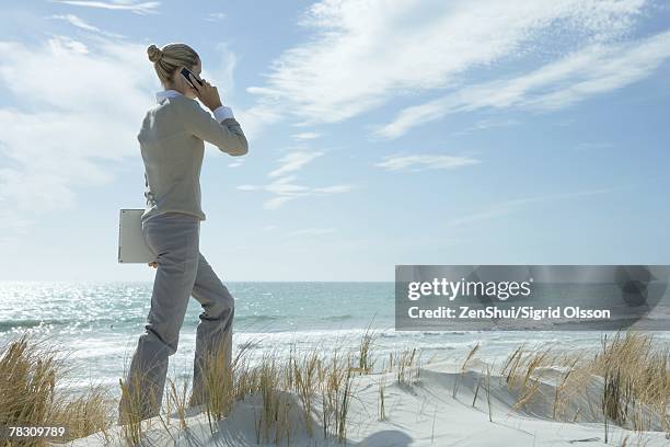 woman walking across dunes, using cell phone, carrying laptop under arm - businesswoman blond looking left foto e immagini stock