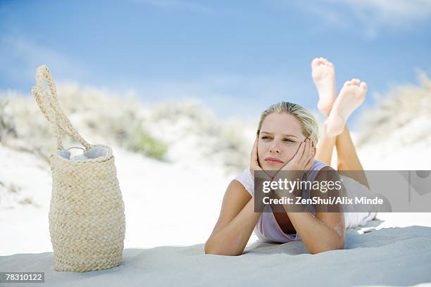 young woman lying on beach, beach bag nearby - hand on chin stock pictures, royalty-free photos & images