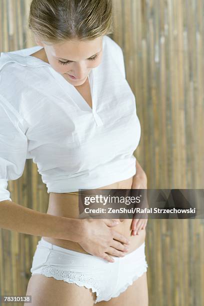 young woman standing with hands on abdomen, looking down, smiling - smiling woman waist up stock pictures, royalty-free photos & images