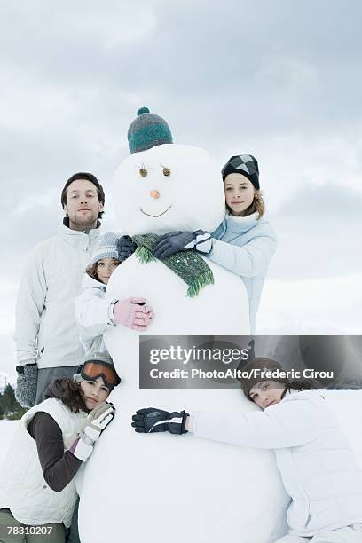 young friends grouped around snowman, posing, portrait - traditional parka stock pictures, royalty-free photos & images