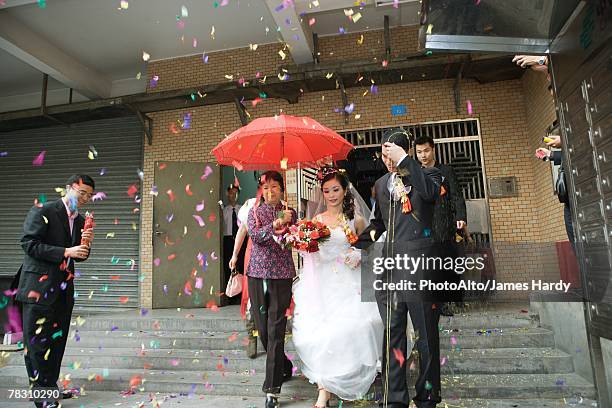 chinese wedding, bride and groom leaving under confetti, bride covered by red parasol - chinese wedding dress stock pictures, royalty-free photos & images