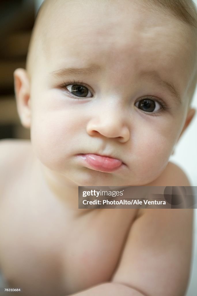 Baby sticking out lower lip and furrowing brow, looking at camera, close-up