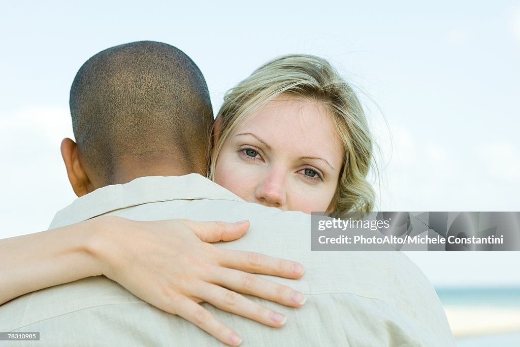 Woman embracing man, looking over his shoulder at camera
