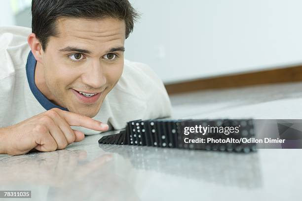 young man knocking over line of dominos - domino effect stock pictures, royalty-free photos & images