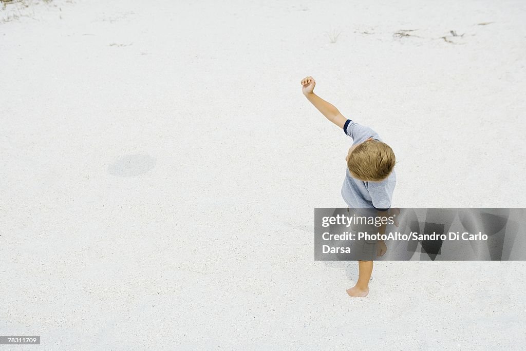 Young boy walking on the beach with one arm raised, high angle view