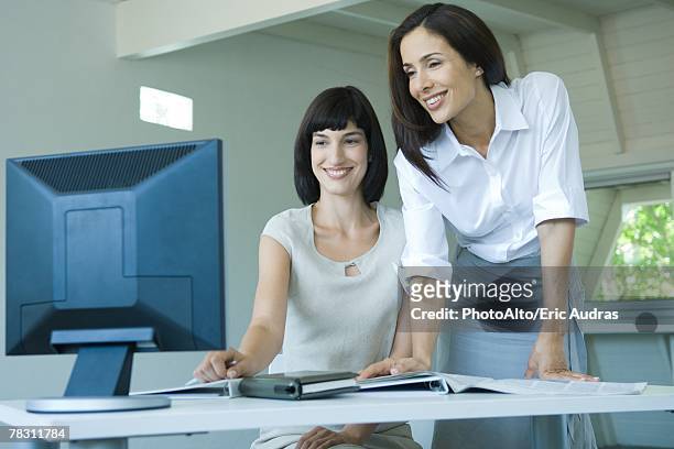two businesswomen looking at computer monitor together, smiling - three quarter front view ストックフォトと画像