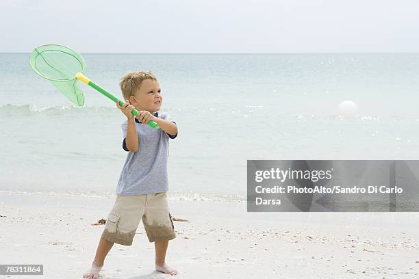 young boy at the beach, holding up net to catch ball - butterfly net stock pictures, royalty-free photos & images