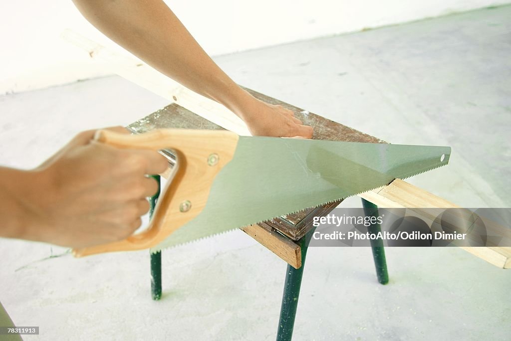 Woman sawing piece of wood, close-up of hands