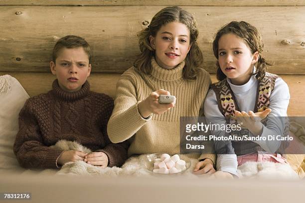 three young siblings watching tv, teen girl changing channel while brother and sister complain - command sisters photos et images de collection