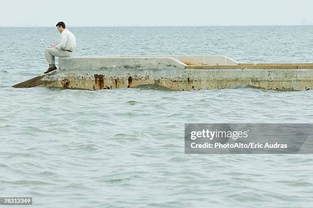 man sitting on pier, using laptop computer, full length, side view - groyne stock pictures, royalty-free photos & images