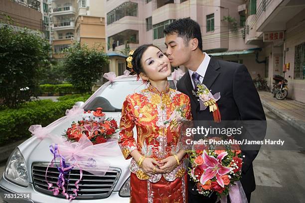 groom kissing bride on cheek in front of car - chinese wedding dress foto e immagini stock