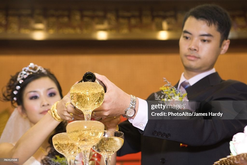 Bride and groom pouring champagne into stacked champagne glasses together