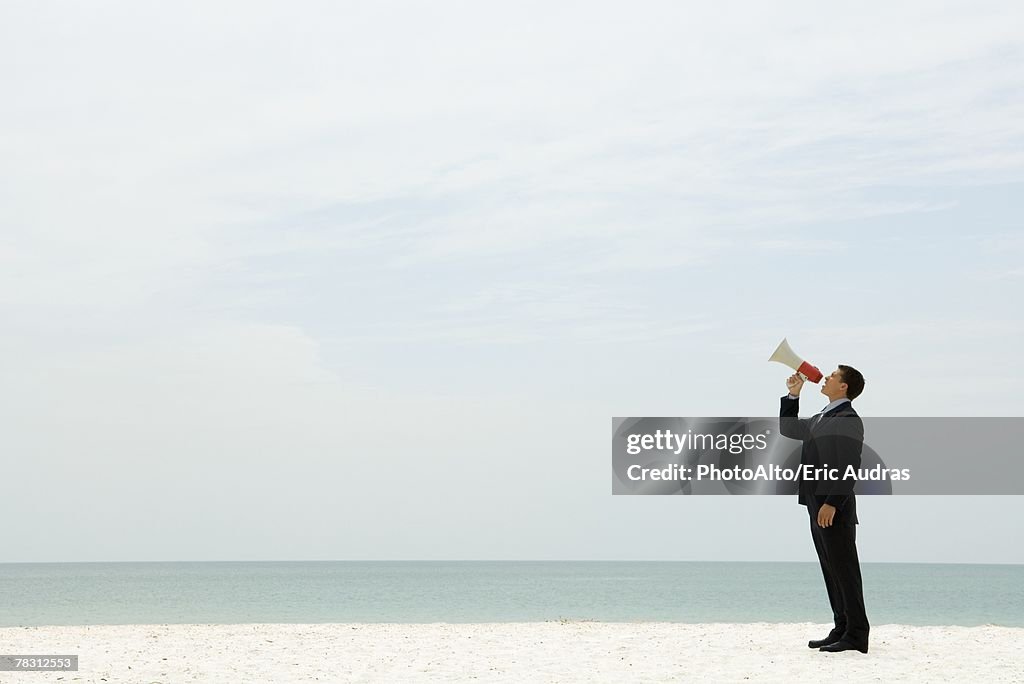 Businessman standing at the beach shouting into megaphone