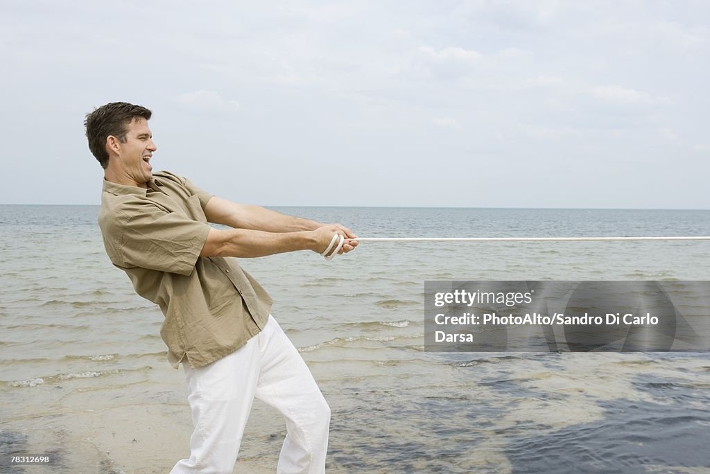 Man playing tug-of-war at the beach, side view