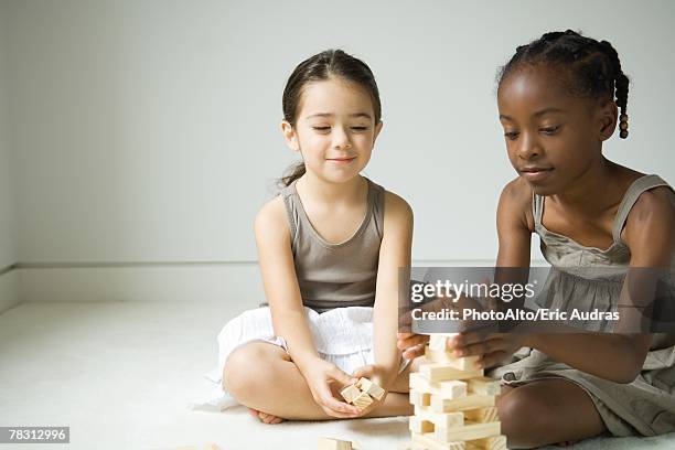 two girls sitting on floor stacking blocks - bending over in skirt stock-fotos und bilder