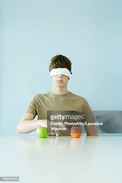 young male wearing blindfold, pointing to one of two apples - occhi chiusi foto e immagini stock