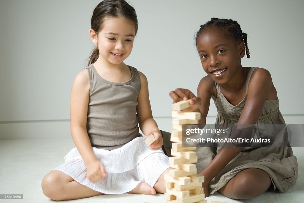 Two girls sitting on floor playing with blocks, one smiling at camera