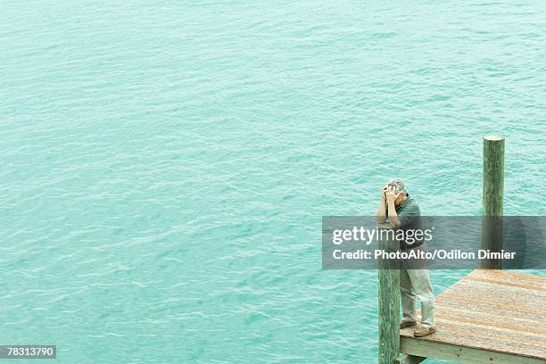 man standing on dock, leaning on post, holding head, high angle view - midlife crisis stock pictures, royalty-free photos & images