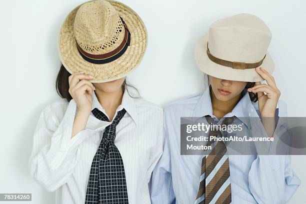 two young friends pulling hats down over their faces, portrait - androgyn stock-fotos und bilder