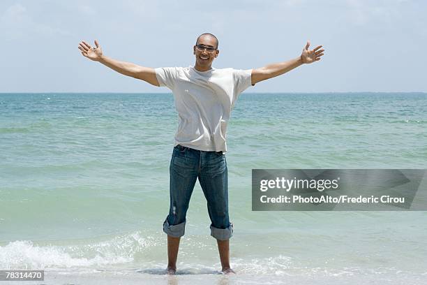 man standing ankle deep in ocean with arms outstretched, smiling at camera - knöcheltief im wasser stock-fotos und bilder