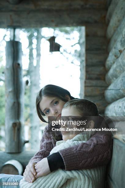 teen girl sitting with arm around younger brother, both wearing warm sweaters - hermano hermana fotografías e imágenes de stock