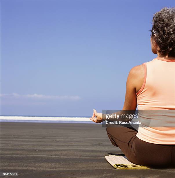 woman meditating on beach - halber lotussitz stock-fotos und bilder