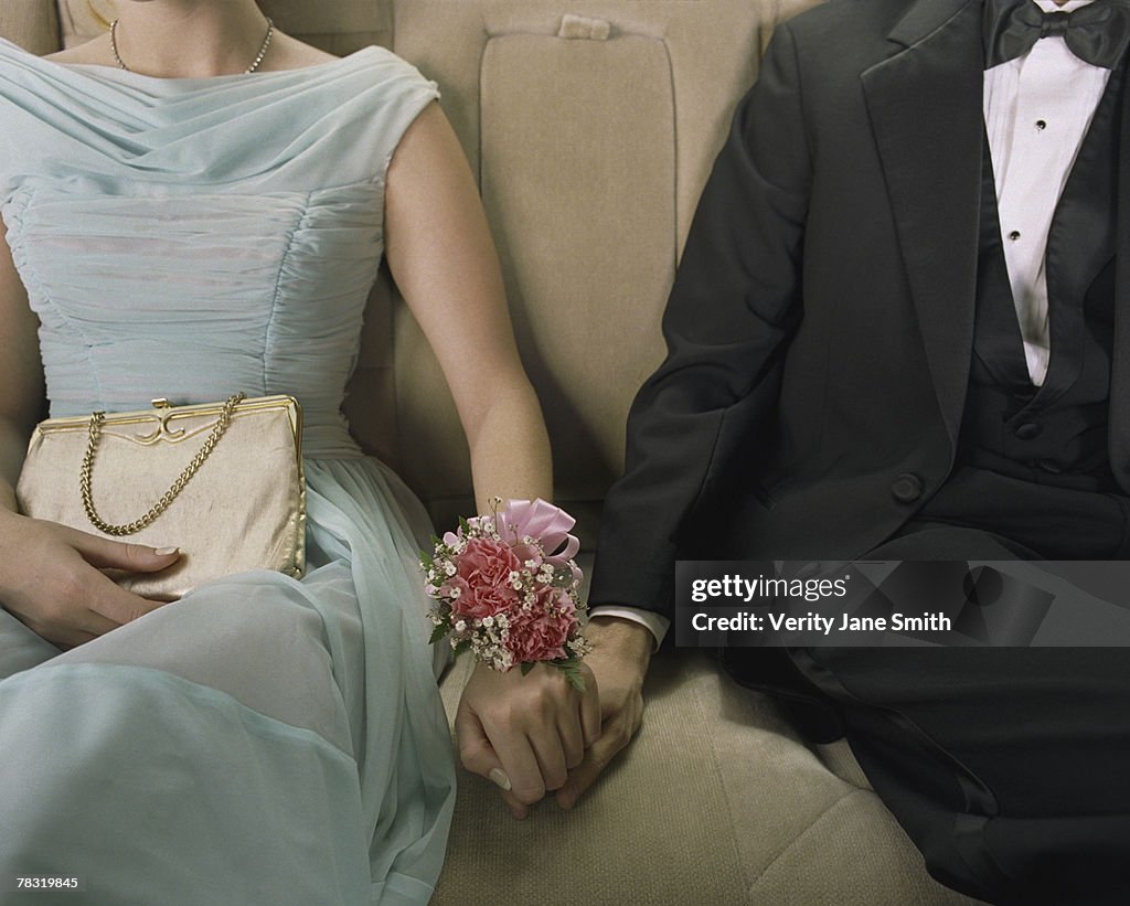 Prom couple holding hands in back seat of car