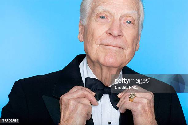 portrait of elderly man straightening bowtie - adjusting blue tie stock-fotos und bilder
