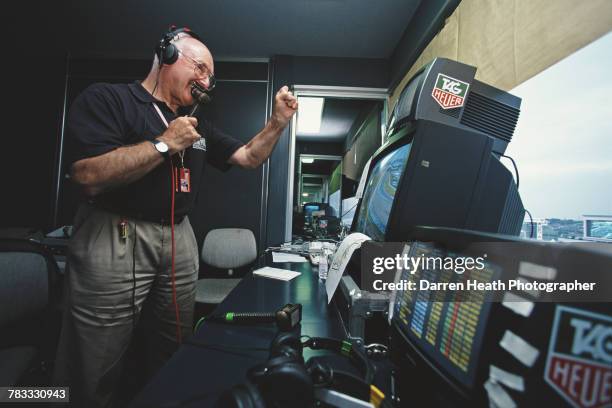 Motorsport television commentator and journalist Murray Walker poses for a portrait with a microphone beside the television monitors in the...