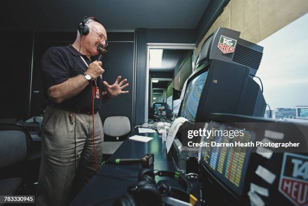 Motorsport television commentator and journalist Murray Walker poses for a portrait with a microphone beside the television monitors in the...