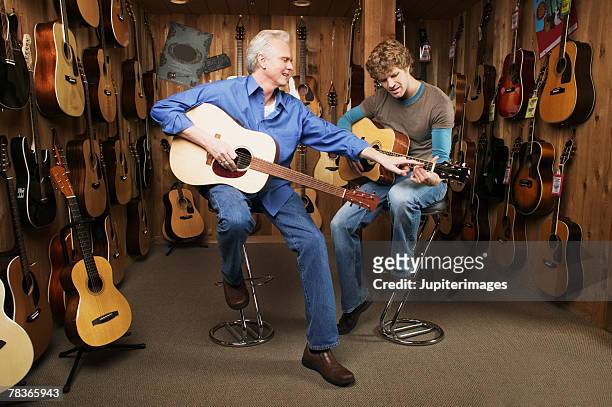 middle-aged man giving guitar lesson to mid-adult man - musikgeschäft stock-fotos und bilder