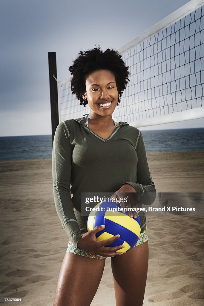 Smiling mid-adult woman holding volleyball on beach