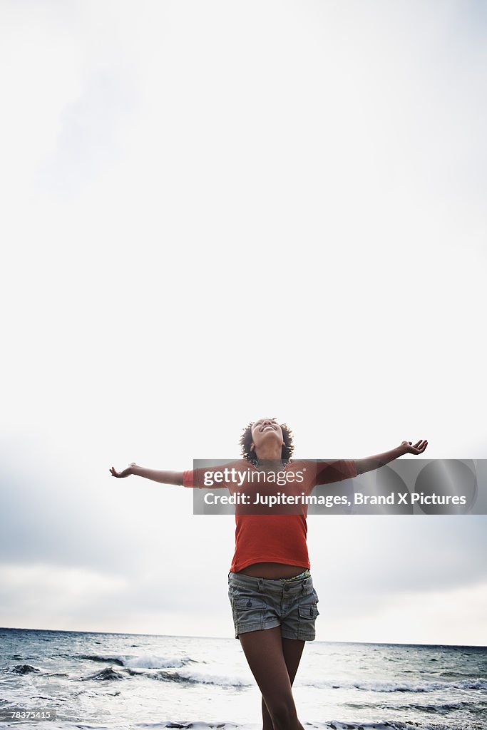 Mid-adult woman standing on beach with arms outstretched