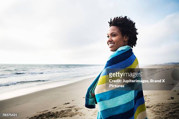 mid-adult woman wrapped in towel on beach - beach towel stock pictures, royalty-free photos & images