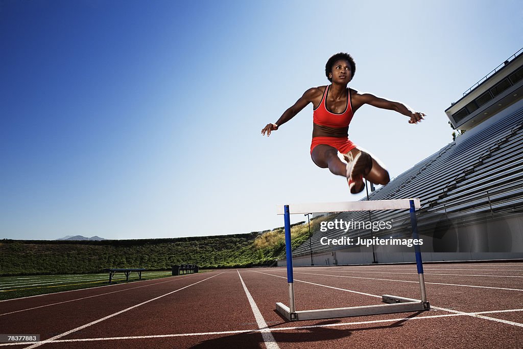 Athletic woman jumping over hurdle