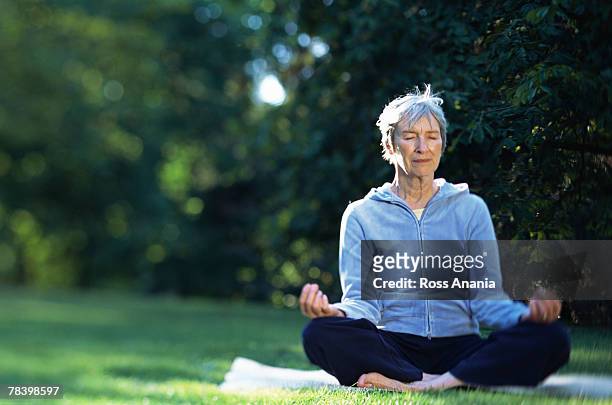 senior woman meditating outdoors - halber lotussitz stock-fotos und bilder