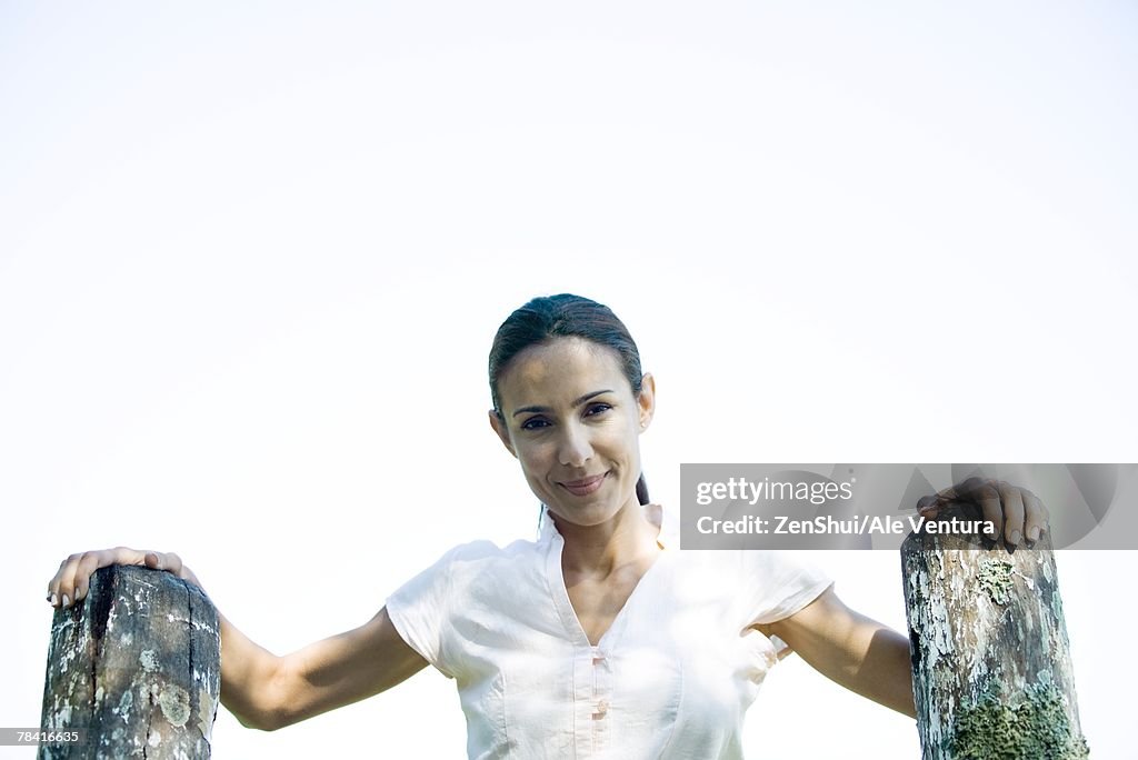 Woman with hands on wooden posts, smiling at camera, low angle view