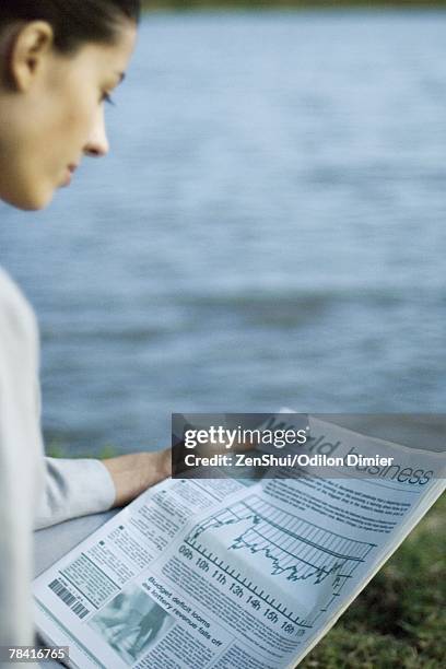 businesswoman reading newspaper, lake in background - westers schrift stockfoto's en -beelden