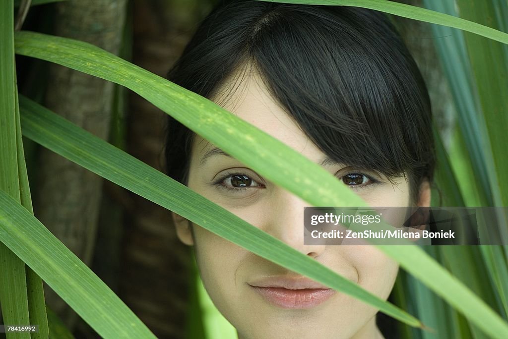 Young woman looking through palm leaf, smiling at camera, portrait