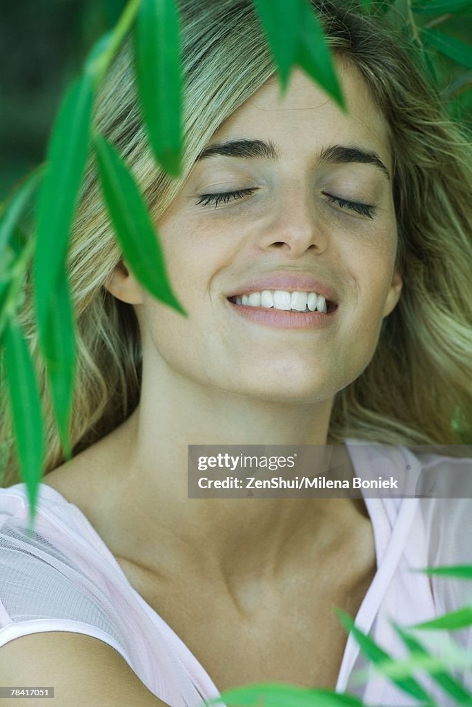 Young woman among foliage, smiling, eyes closed, portrait