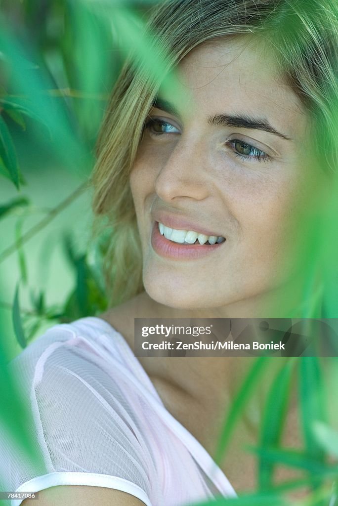 Woman smiling, looking away, blurred vegetation in foreground