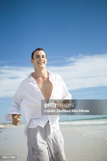 young man running on beach, smiling - button down shirt stock pictures, royalty-free photos & images