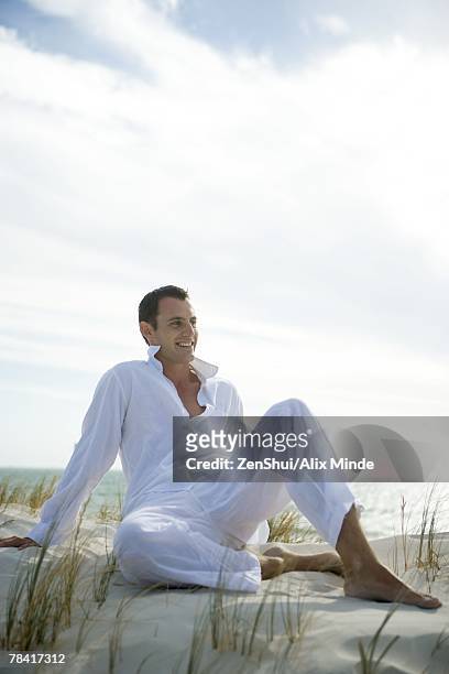 young man sitting on dune, smiling, full length - linen shirt stock pictures, royalty-free photos & images