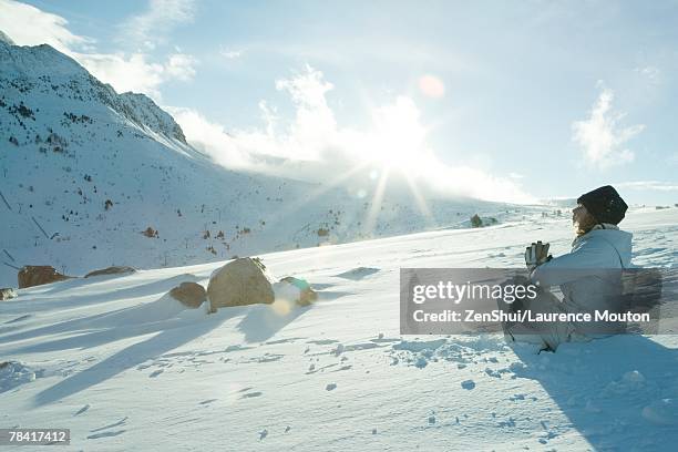 teen girl sitting on snow in prayer position, sun shining over edge of mountain - yoga in the snow stock-fotos und bilder