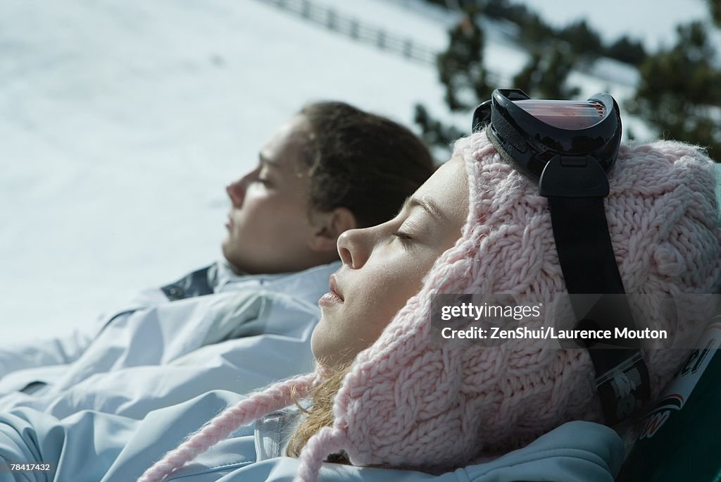 Teen girls sitting in chairs in snowy landscape, relaxing in sun, close-up