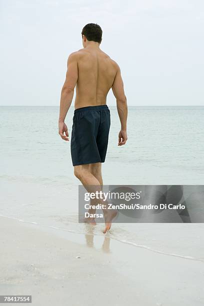 man walking in surf, rear view - badehose stock-fotos und bilder