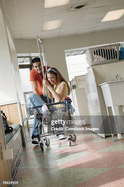 man pushing woman in cart at laundry facility - man pushing cart fun play stock pictures, royalty-free photos & images