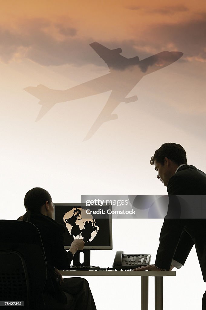 Two businessmen at computer with airplane travel graphics
