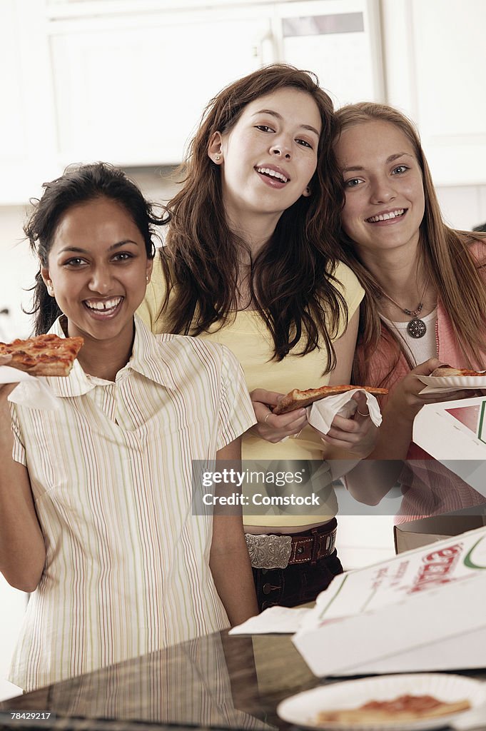 Teenage girls eating pizza together in kitchen